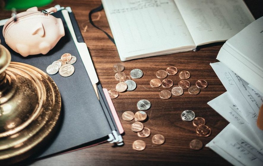 Caderno de anotações e moedas organizados sobre a mesa, representando o controle manual de contas e vencimentos